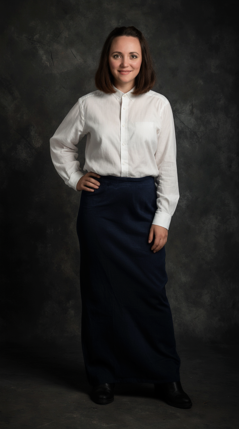 krea.ai für anfänger: Frau steht vor einem dunklen Fotostudio-Hintergrund. Sie trägt ein weißes, geknöpftes Hemd und einen langen dunklen Rock. Eine Hand liegt an der Hüfte, sie lächelt dezent.