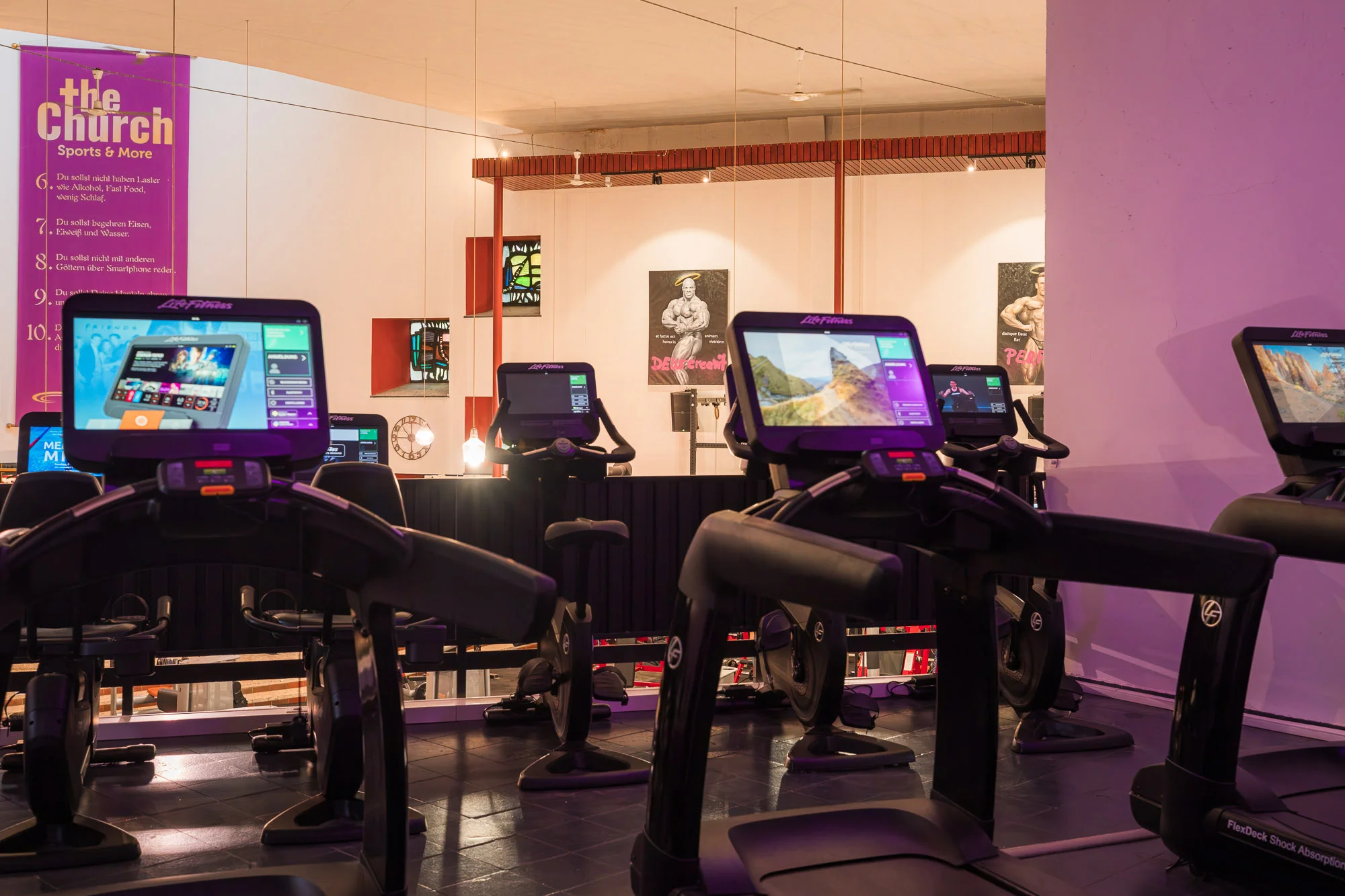 ava_202603124 Reihe von Cardio-Geräten mit Bildschirmen im Fitnessstudio zur Umsetzung eines Trainingsplans von ChatGPT.