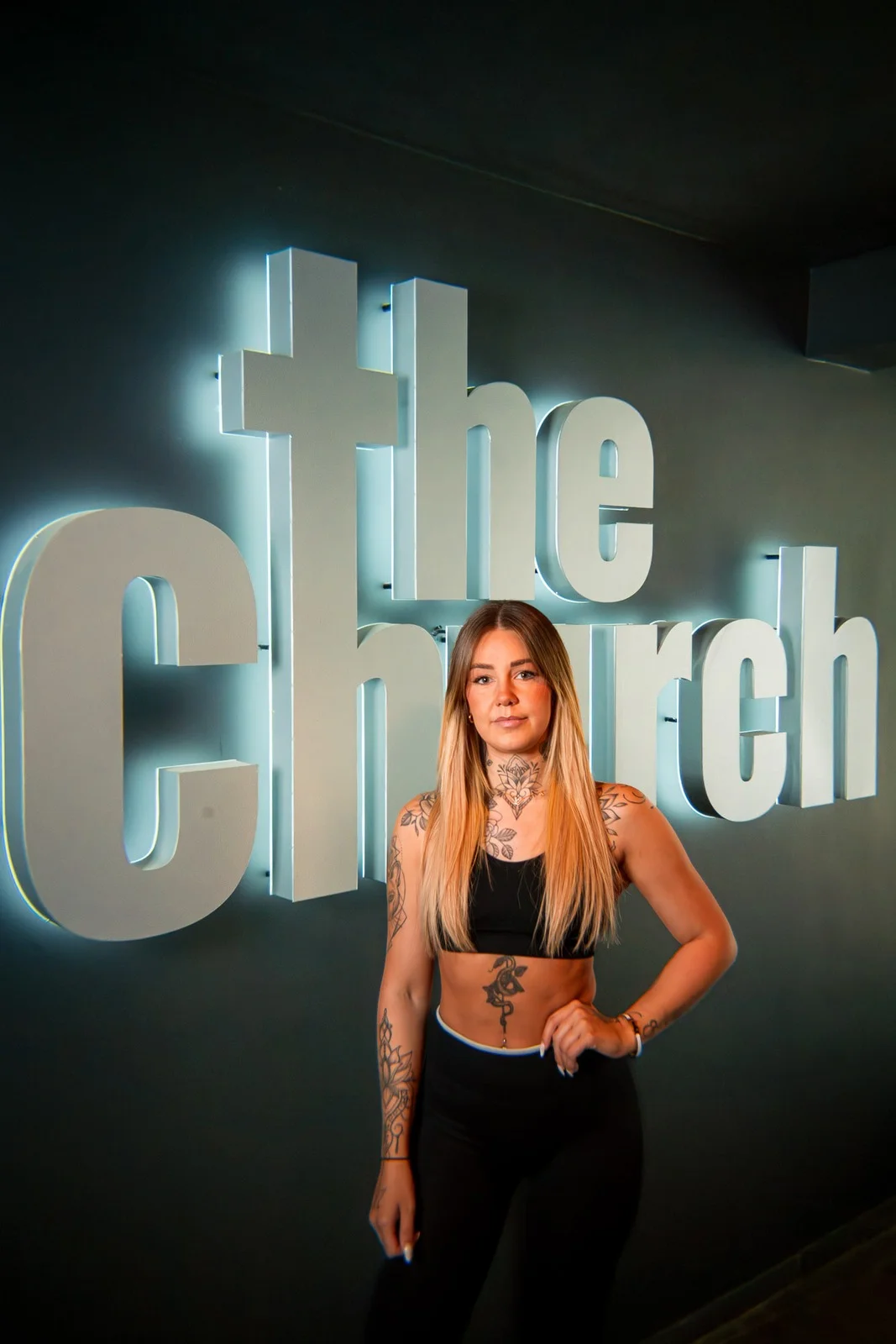 ava_202603126 Sportliche Frau posiert vor dem leuchtenden „The Church“-Logo